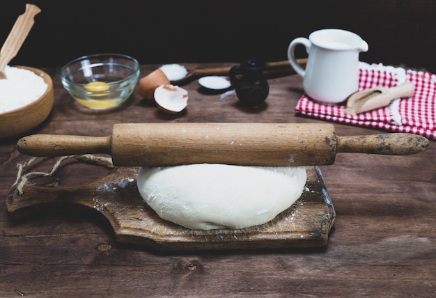 Piece of white wheat flour dough on a brown board 