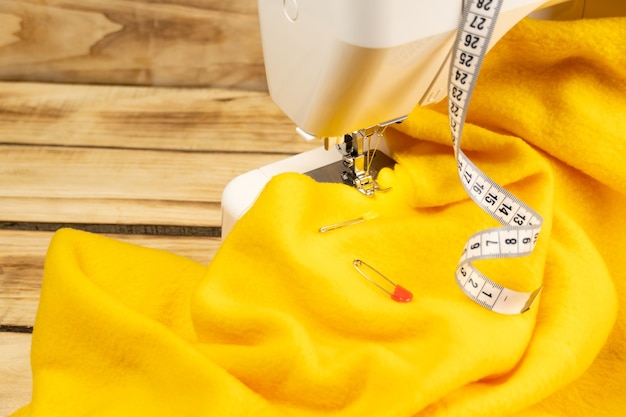 Кусок желтой ткани на швейной машинке и сантиметр на деревянном фоне