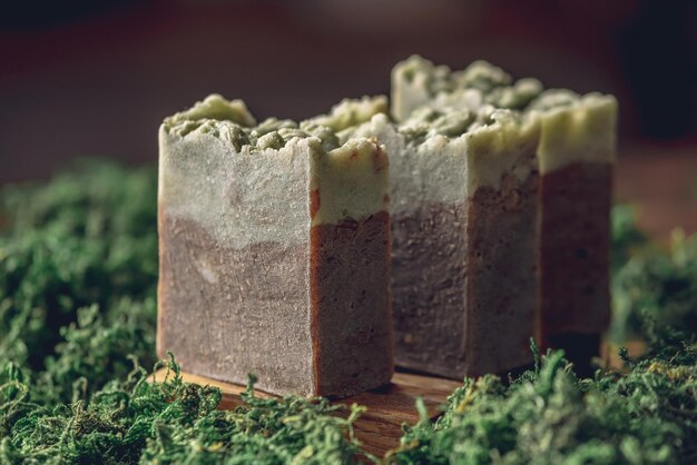 Pieces of authentic craft organic soap on a wooden soap dish surrounded by green moss Concept of natural cosmetics made from safe eco friendly ingredients