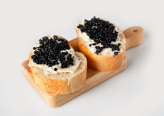 Pieces of baguette with butter and halibut caviar on a wooden board on a white background