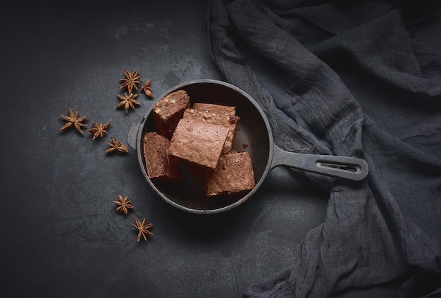 Pieces of baked brownie in a metal black frying pan on the table, top view