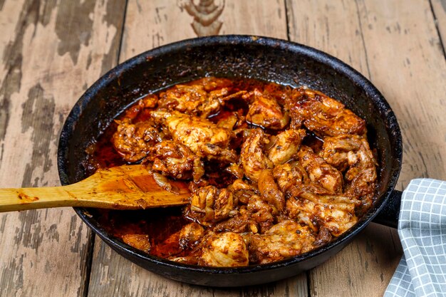 Pieces of baked chicken in sauce in a frying pan with a wooden spatula