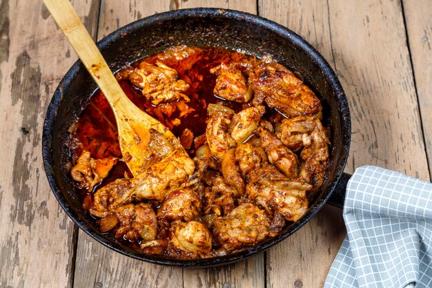 Pieces of baked chicken in sauce in a frying pan with a wooden spatula