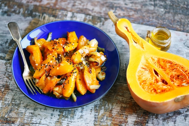 Pieces of baked pumpkin with onions on a blue plate Pumpkin recipe Autumn food