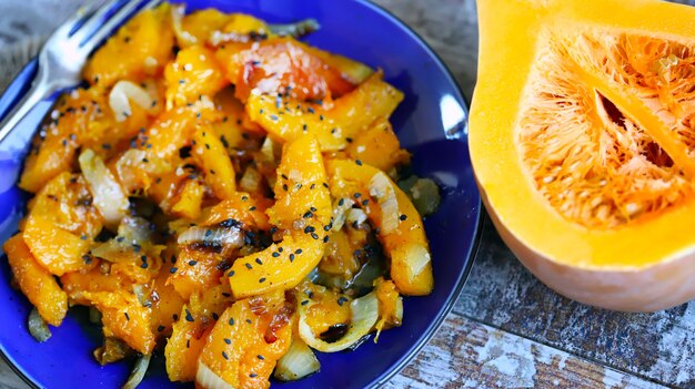 Pieces of baked pumpkin with onions on a blue plate Pumpkin recipe Autumn food