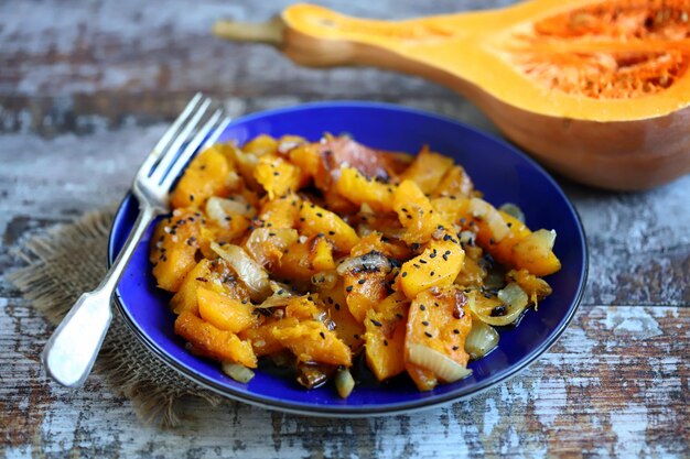 Pezzi di zucca al forno con cipolle su un piatto blu