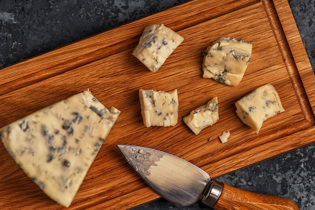Pieces of blue cheese on wooden serving board, top view
