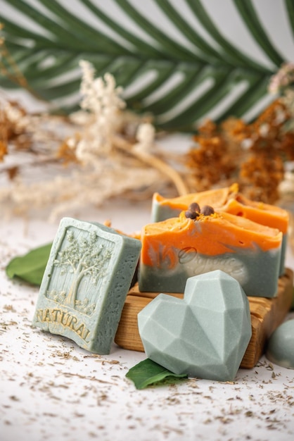 Pieces of bright natural handmade soap on a wooden soap dish with green leaves around