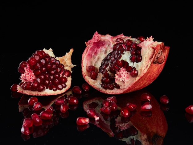 Pieces of broken pomegranate fruit on a black glossy background