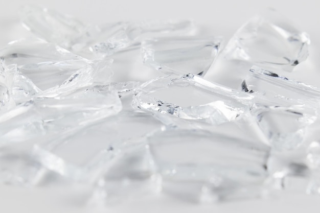 Pieces of broken transparent glass on white surface close up