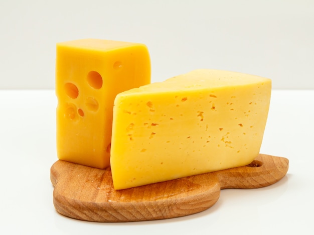 Pieces of cheese on a wooden cutting board in the white surface