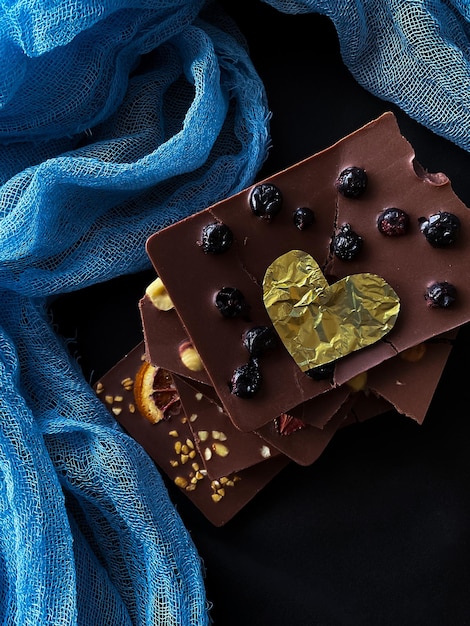 Photo pieces of chocolate with golden foil heart with berries strawberries oranges