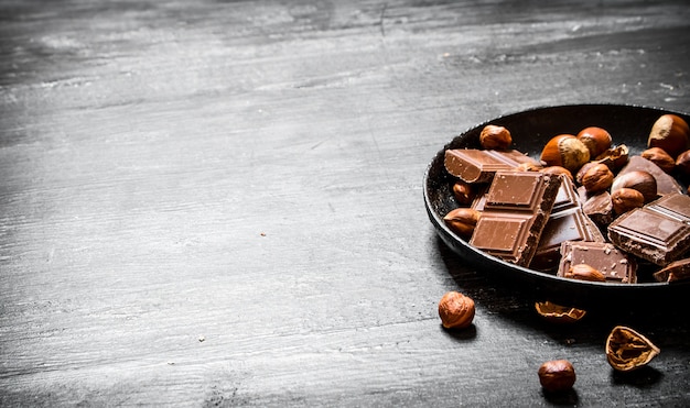 Photo pieces of chocolate with nuts on the old plate. on the black wooden table.