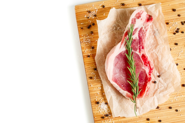 Фотография кусочки сырого мяса с розмарином и специями на деревянной разделочной доске