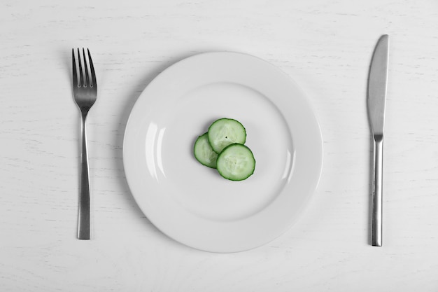 Photo pieces of cucumber in a white plate on white table top view