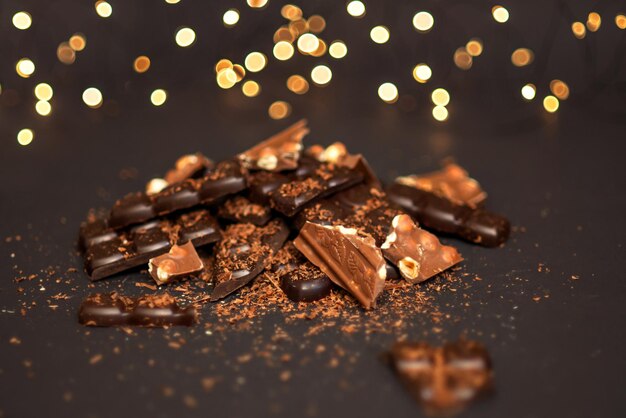 Pieces of dark and milk chocolate lie in a pile on a dark paper background