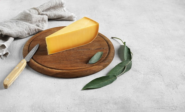 Pieces of delicious parmesan cheese on wooden board and sage leaves against white background space f