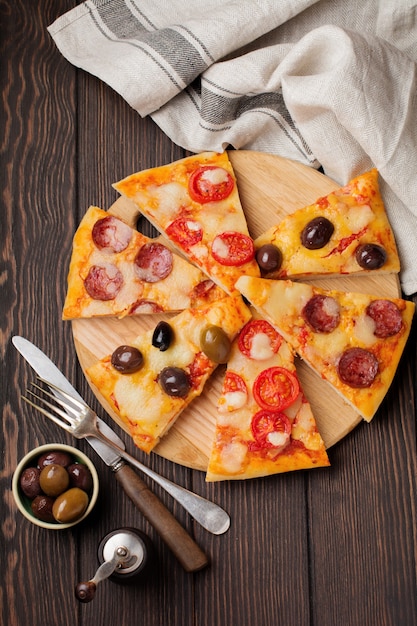 Pieces of different Greek pizzas with olives, Italian Margarita and Pepperoni on a dark wooden rustic.   