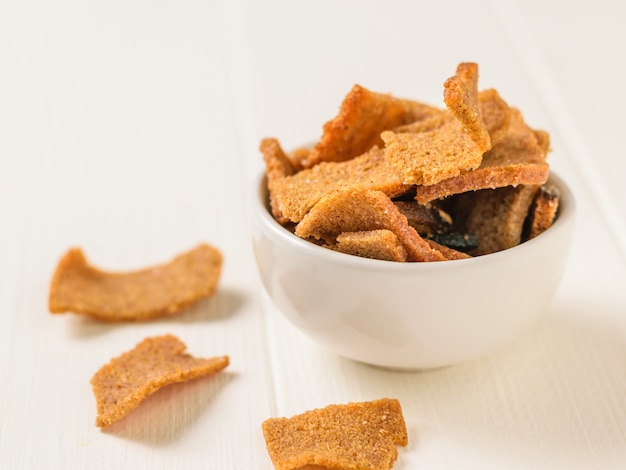 Pieces of dried bread in a white bowl on rustic wooden table.