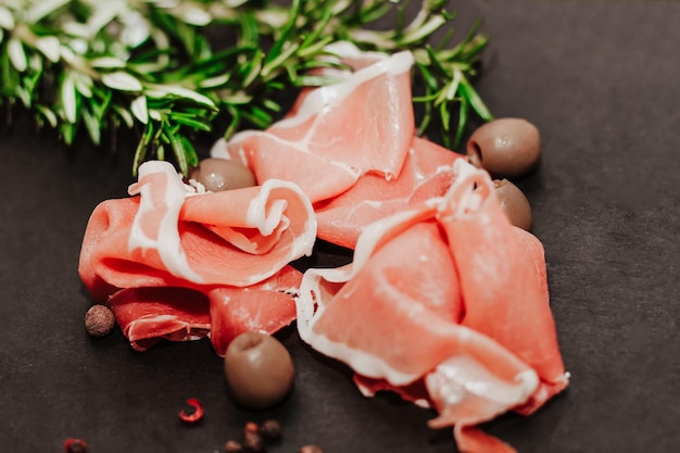 Pieces of dried pork jamon prosciutto with olives on a black board