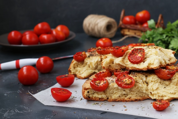 Pieces of focaccia with cherry tomatoes are located on parchment on a dark surface