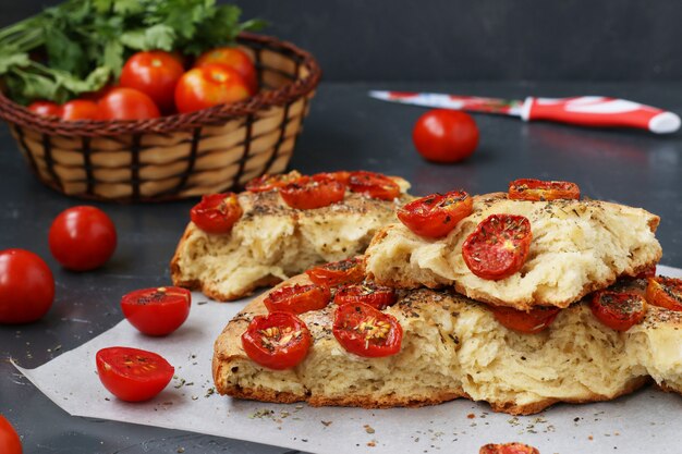 Pieces of focaccia with cherry tomatoes are located on parchment on a dark surface