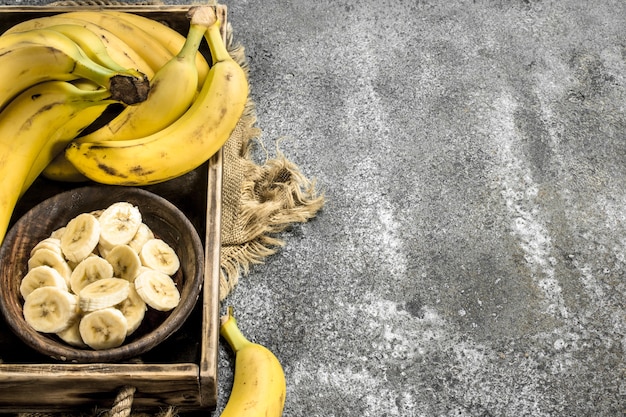 Photo pieces of fresh bananas in a bowl on tray on rustic table.