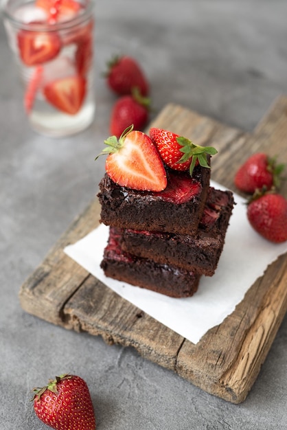 Pieces of fresh chocolate brownie with strawberries on a concrete background