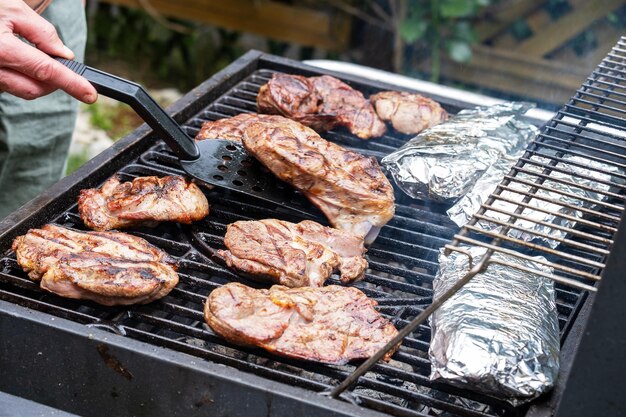 Pieces of fresh raw meat laid out on grill grate Barbecue cooking Hand of an unrecognizable person flips the steaks Selective focus