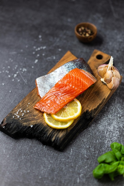 Pieces of fresh trout fish on a burnt wooden board Lemon spices and herbs for cooking