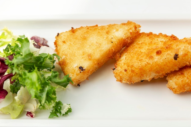 Photo pieces of fried cheese with lettuce on a white plate. appetizing starter. close-up.