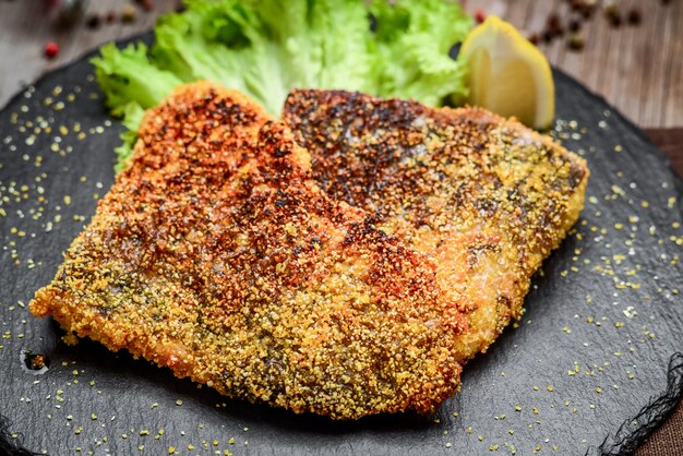 Pieces of fried fish on a ceramic plate on a dark wooden surface