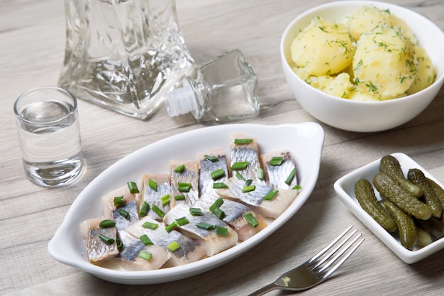 Pieces of herring with onions, gherkins, boiled potatoes and vodka. Selective focus