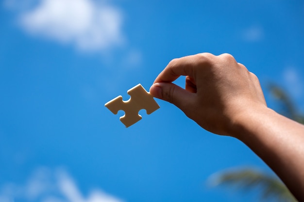 Pieces of jigsaw puzzle in woman's hands with blue sky 