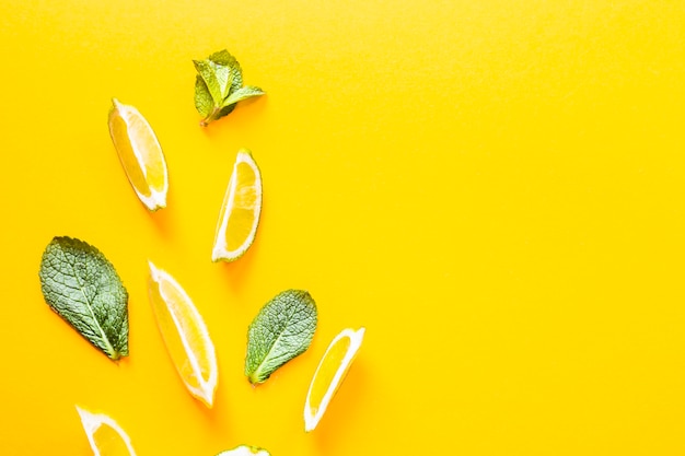 Pieces of lemon, lime and green mint leaves on a yellow background. 