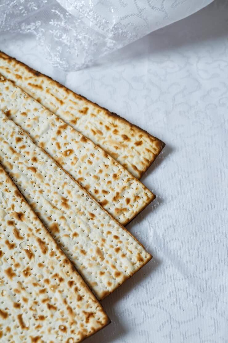 Фотография кусочки маццо - вид безквасного хлеба, неотъемлемой части еврейской пасхи. маццо светло-коричневого цвета с обгоревшими пятнами, указывающими на его печеную природу. маца расположена на белой текстурированной поверхности.