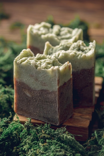 Фото Кусочки подлинного ремесленного органического мыла на деревянной мыльной тарелке, окруженной зеленым мохом концепция естественной косметики, изготовленной из безопасных экологически чистых ингредиентов