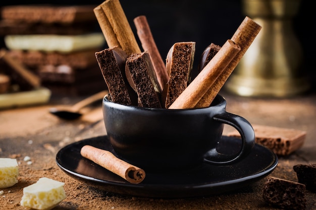 Кусочки пористого шоколада и палочки корицы в черной кофейной чашке