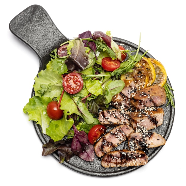 Pieces of organic grilled tuna steak on black ceramic serving dish with salad isolated