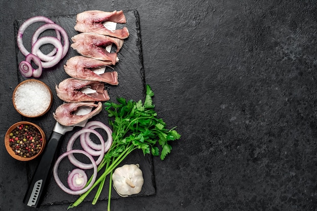 pieces of pickled herring on a knife with onions and herbs on a stone table