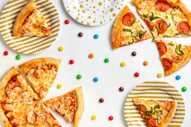Photo pieces of pizza and colored sweets on a white background. birthday with junk food. children's party. top view with copy space for text. flat lay