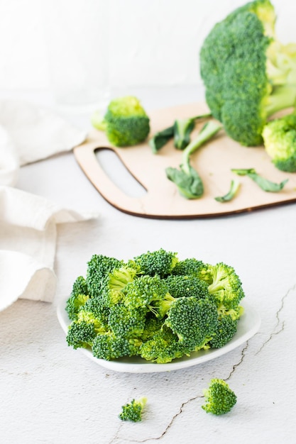 Pieces of raw broccoli on a plate on a light table Cooking healthy vegetarian food Vertical view Closeup