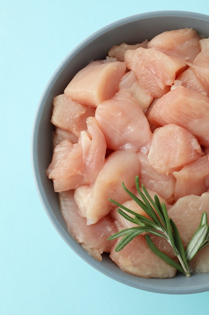 Pieces of raw chicken fillet in bowl on blue background