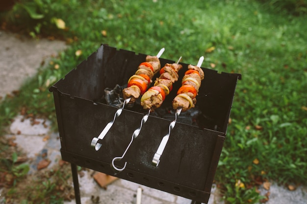 Photo pieces of raw chopped meat with tomatoes and onion rings are cooking on barbecue