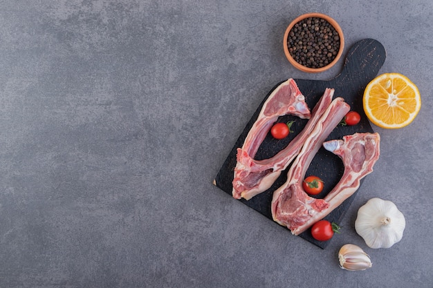 Pieces of raw lamb limbs placed black cutting board.