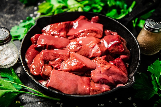 Pieces of raw liver in a frying pan with parsley and spices