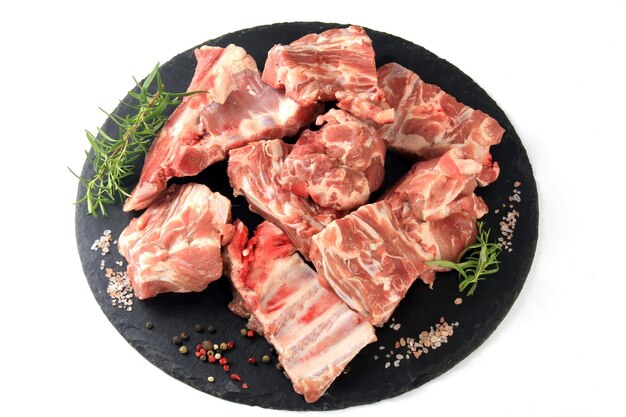 Кусочки сырого мяса на круглой черной каменной тарелке на белом фоне, свежее мясо с костями