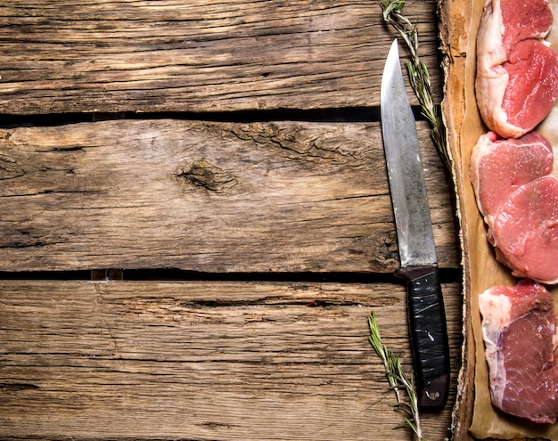 Pieces of raw meat with a butcher knife. On wooden background. Free space for text . Top view