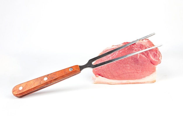 白い背景の上の肉フォークと生のローストビーフ肉の部分グリル用の新鮮な牛肉