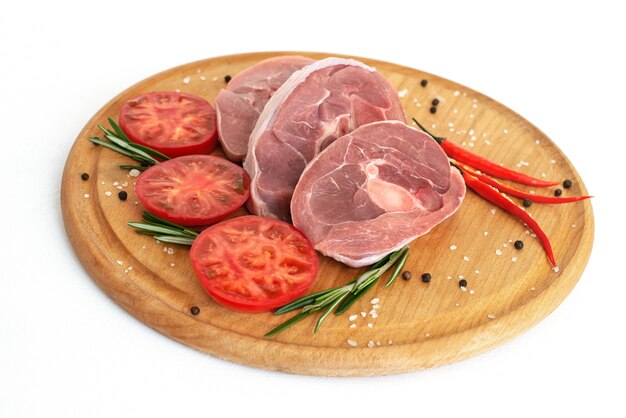 Pieces of raw turkey meat, chopped leg steak, portioned barbecue pieces, on a round wooden board and and a white background with a sprig of rosemary, tomatoes and red hot pepper. isolate.